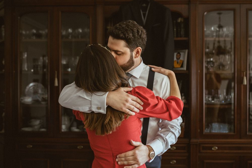 A couple in formal attire dance together in an intimate moment in front of wooden furniture and display cases.