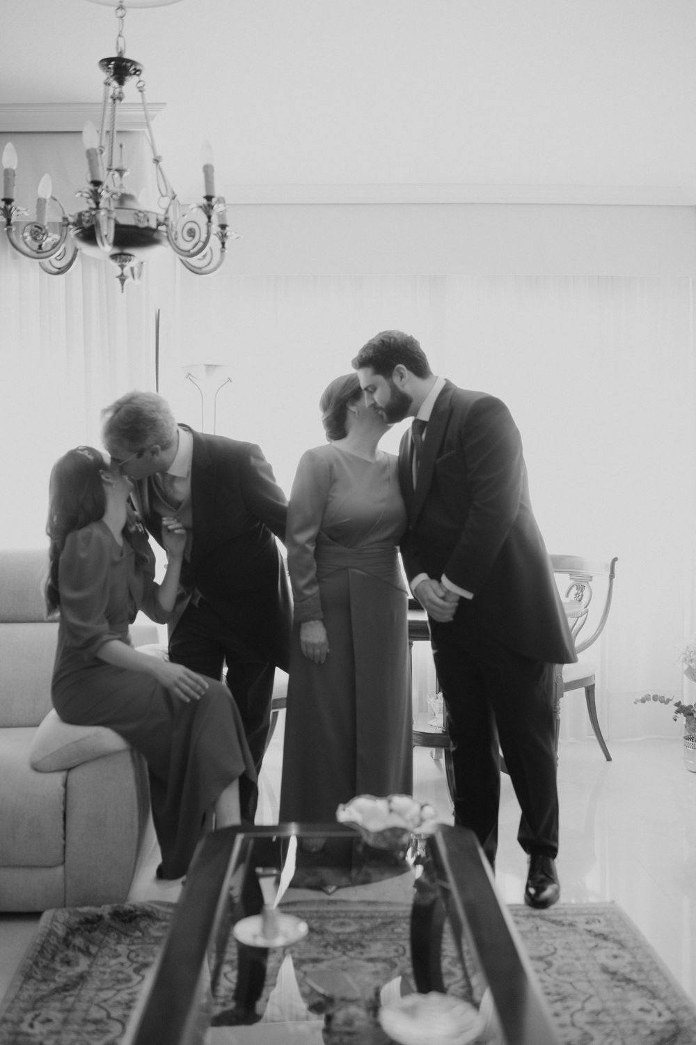 Black and white sequence showing people bending down to examine something on the floor in an elegant room with chandeliers.