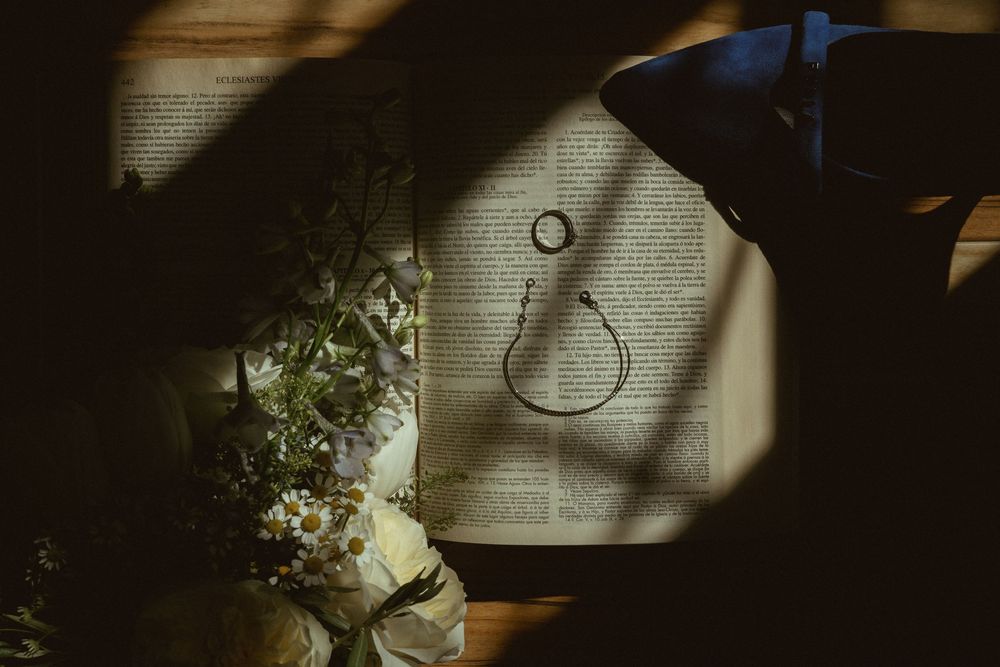 Wedding ring casts shadow on white paper beside delicate floral arrangement in dramatic lighting.