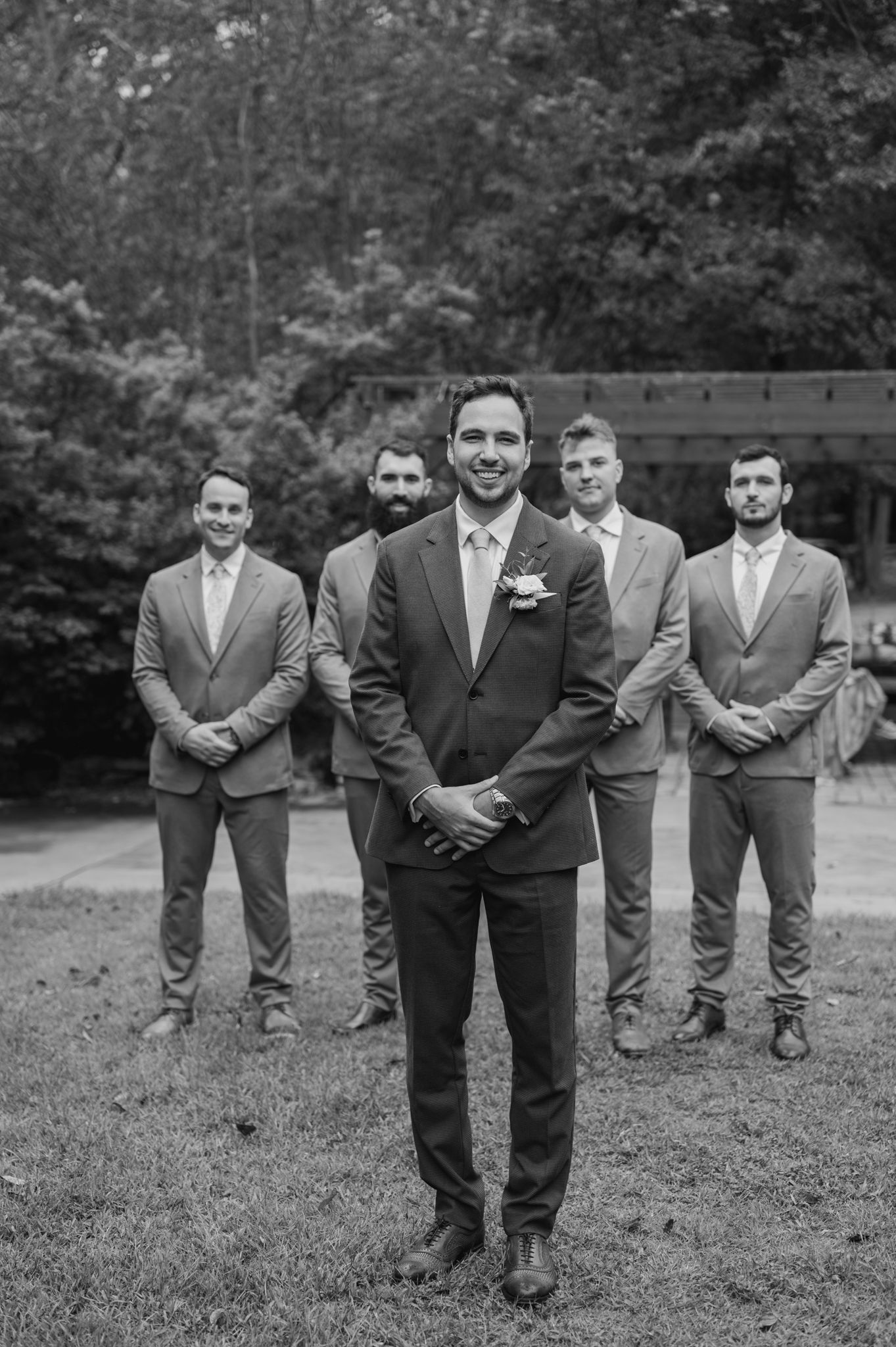 Groomsmen pose playfully in formal suits for wedding party photos.