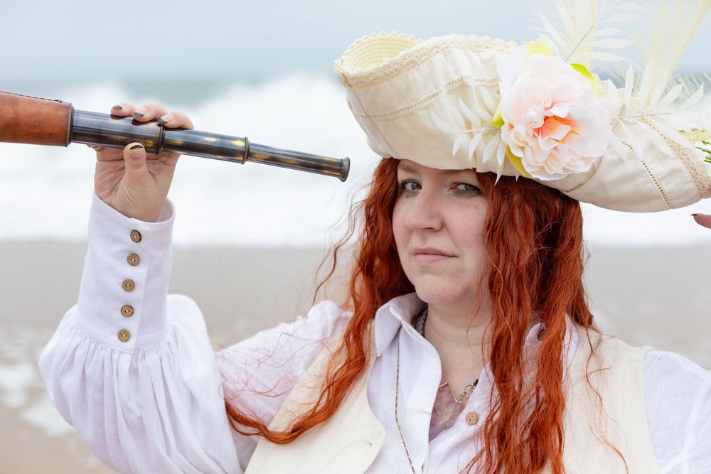 A pirate with ling red hair and a while har looks through a telescope