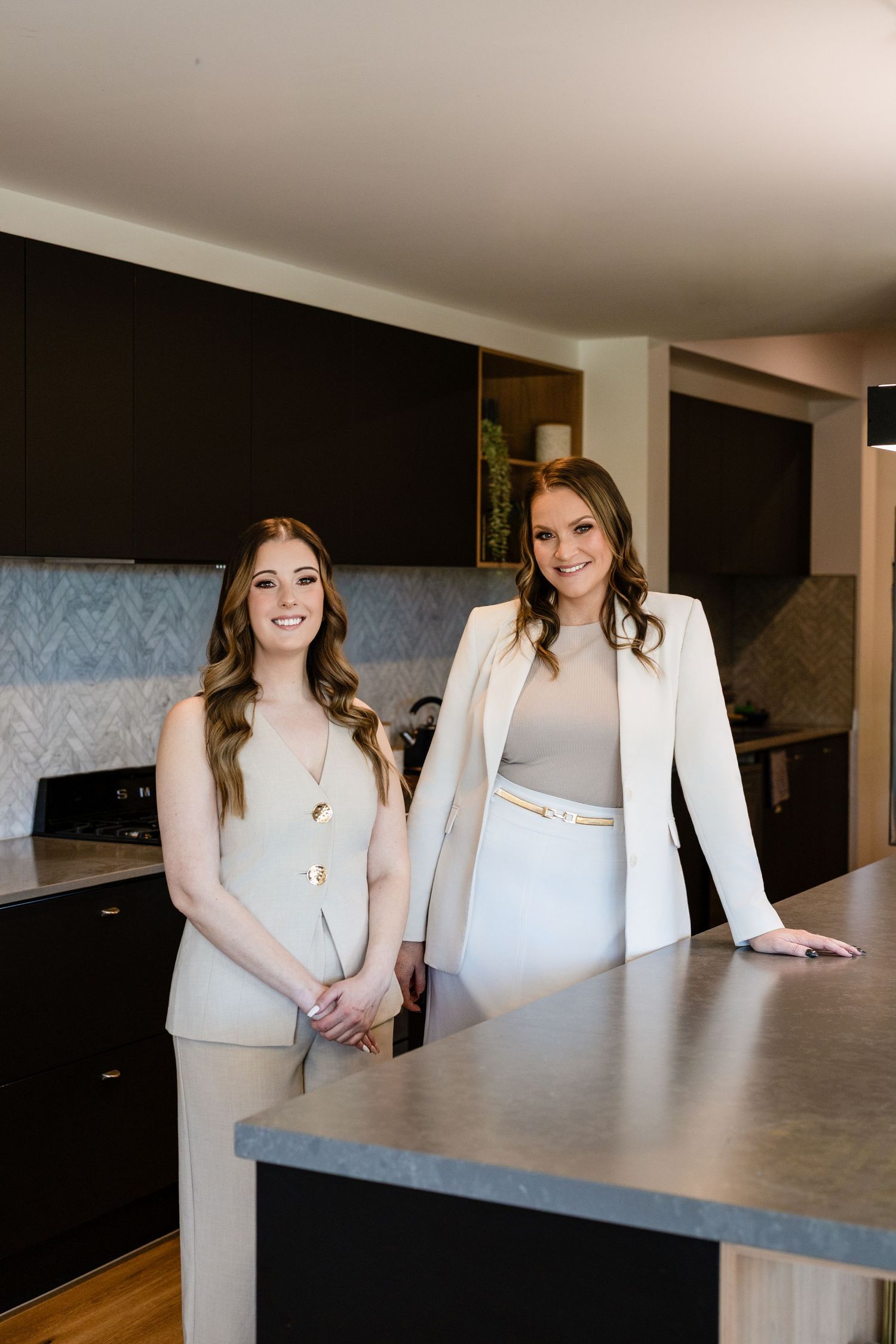 Two people in white tops sit at a modern concrete countertop in a contemporary kitchen setting.