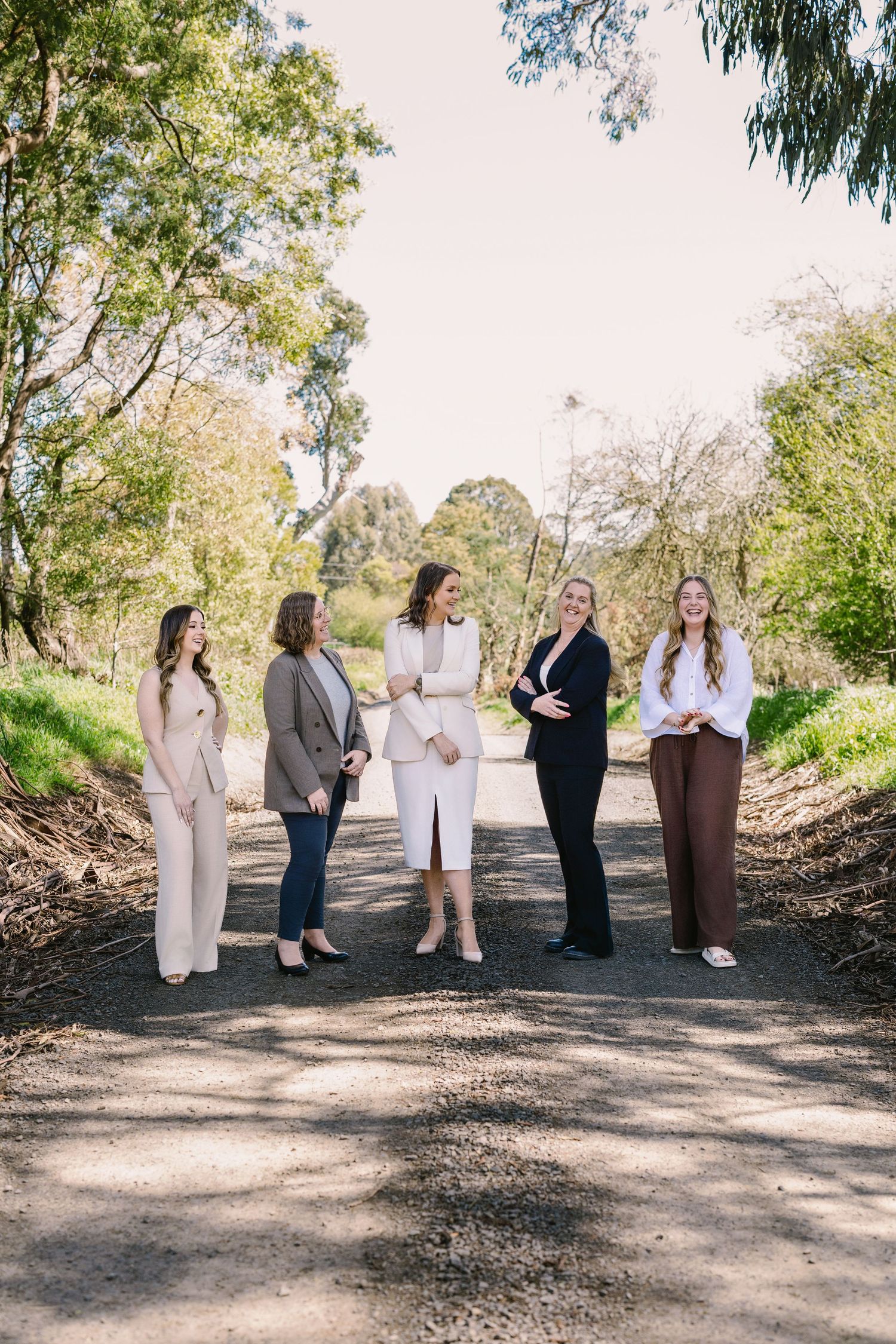 Group of professionals in business attire stand together on a tree-lined path for an outdoor meeting.