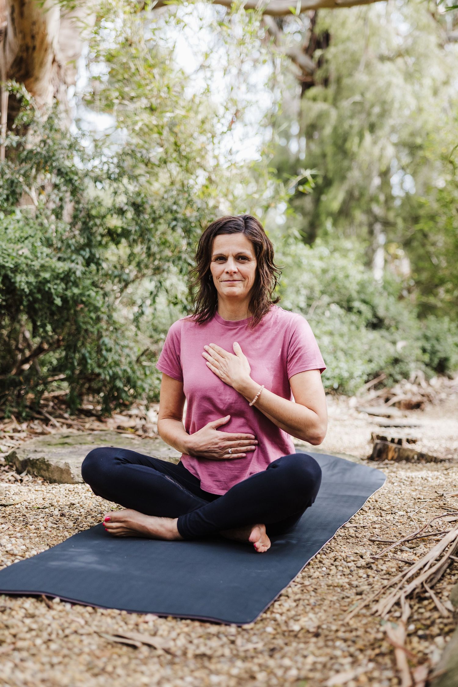 Person practicing yoga or meditation on a black mat in a natural outdoor setting.