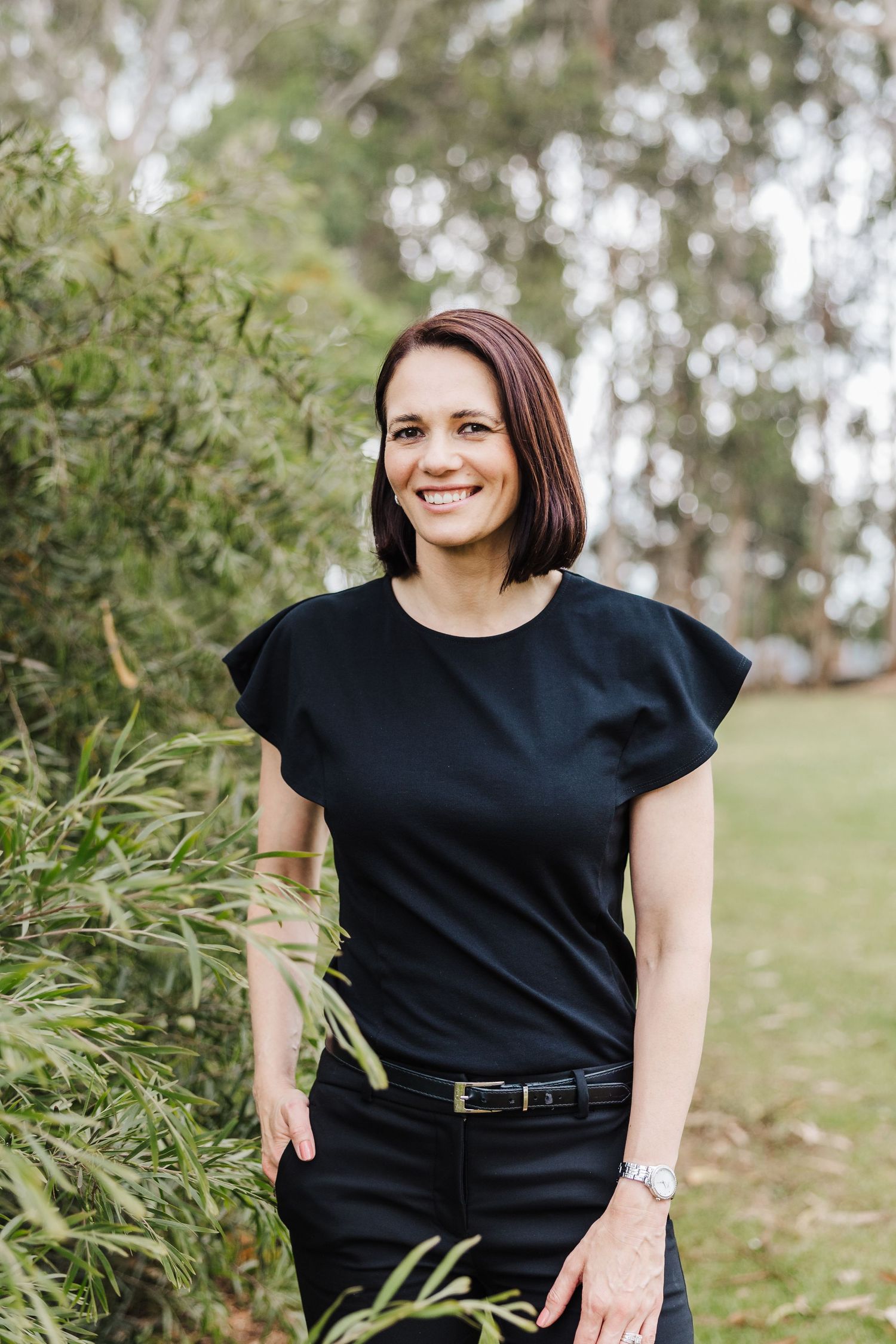 Professional outdoor portrait featuring a black short-sleeve top and dark hair against a natural blurred background.