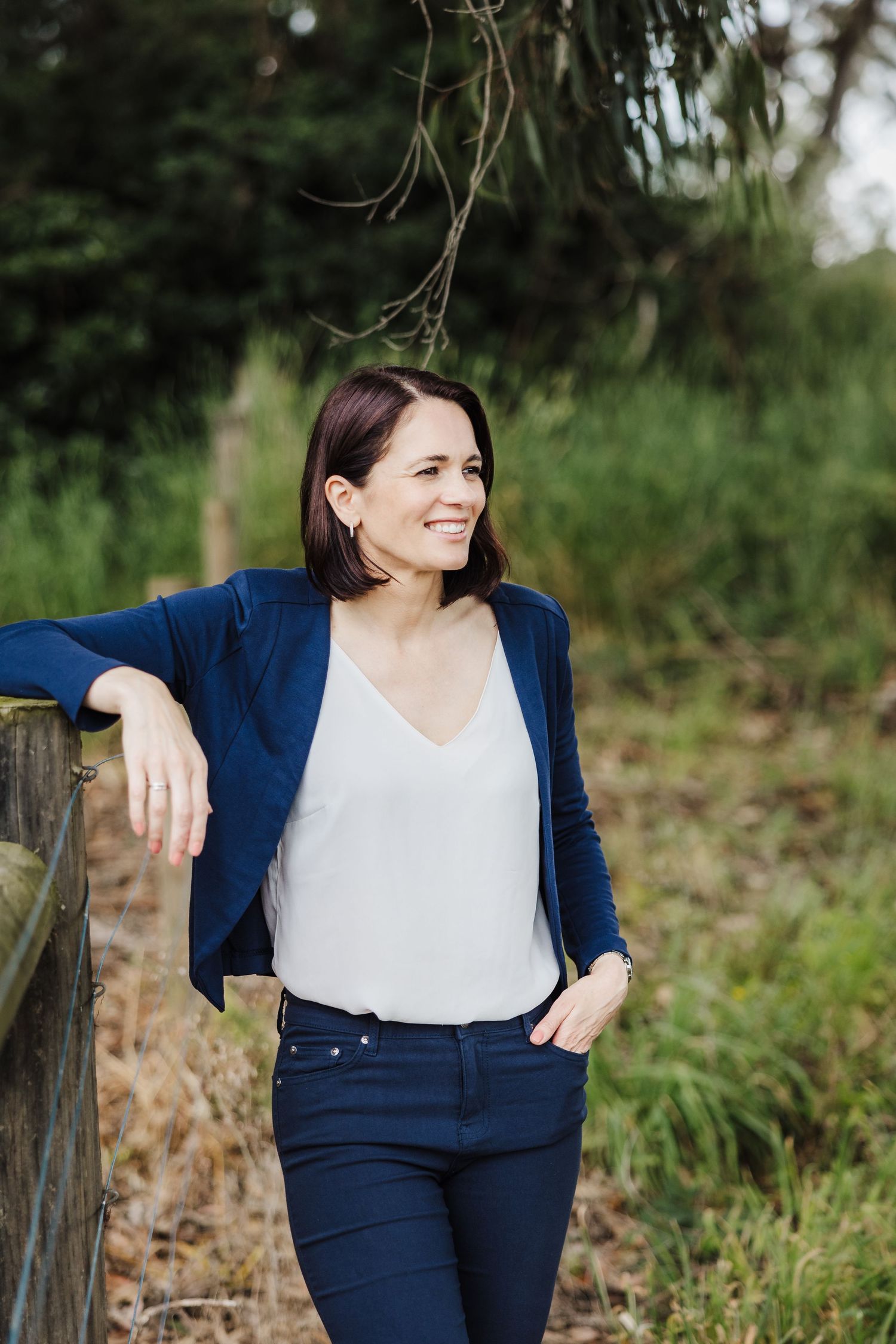 Casual outdoor portrait with a navy blazer, white top and dark jeans in a natural garden setting.