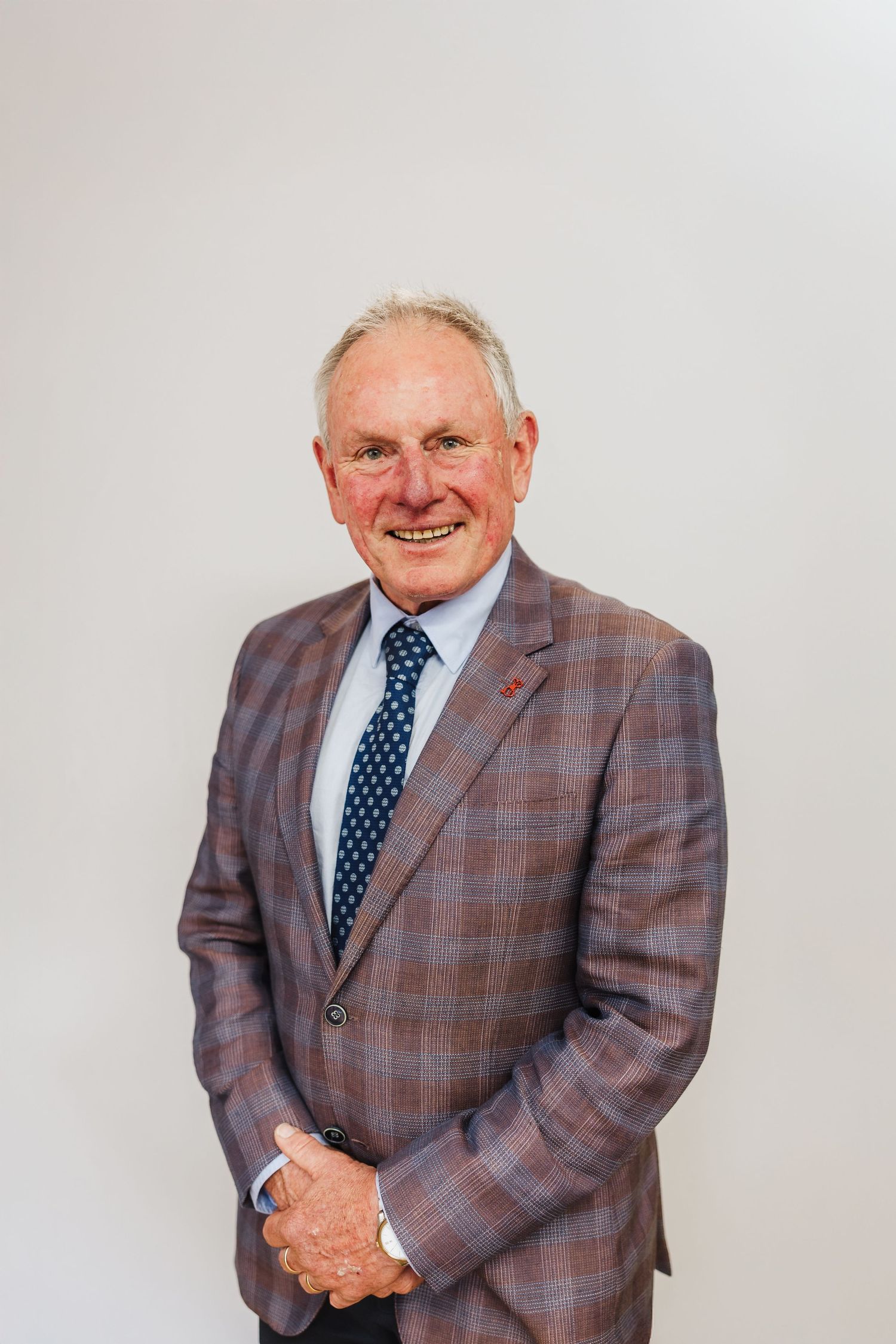 Professional headshot of person in plaid suit jacket and polka dot tie against neutral background.