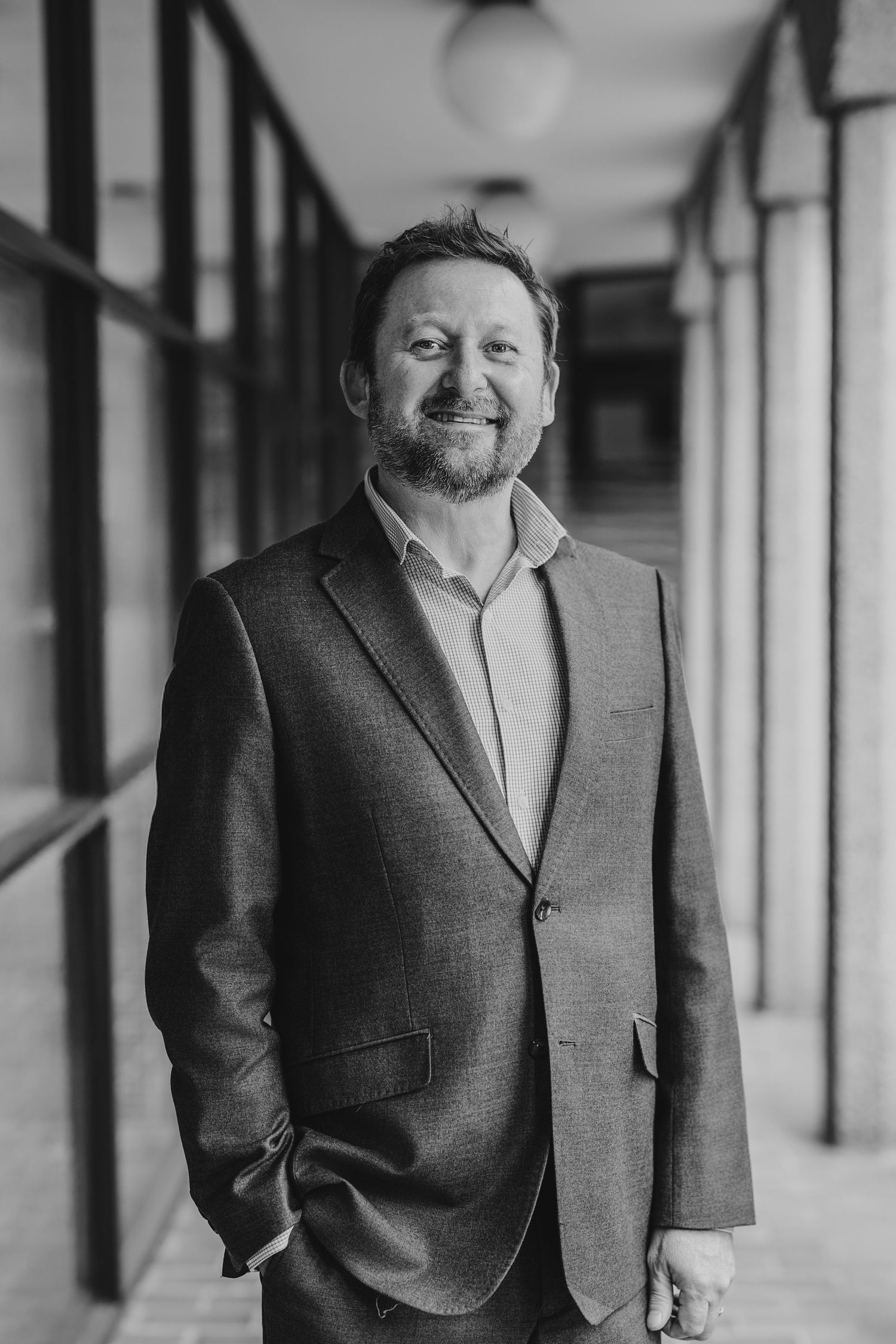 Professional black and white portrait of a person in business attire standing in a hallway with columns.