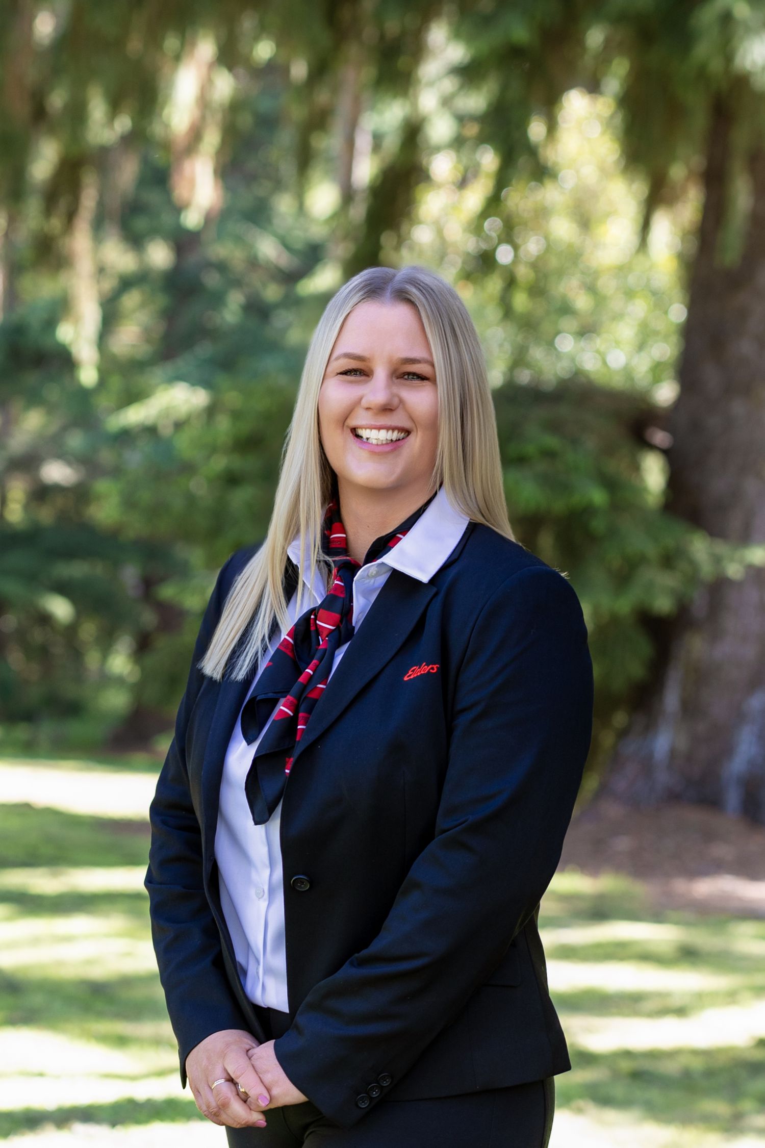 Professional headshots of a person in business attire smiling outdoors with natural lighting and trees in background.