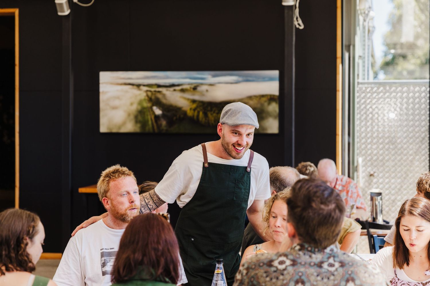 Restaurant server in black apron interacting with customers at a dining table.