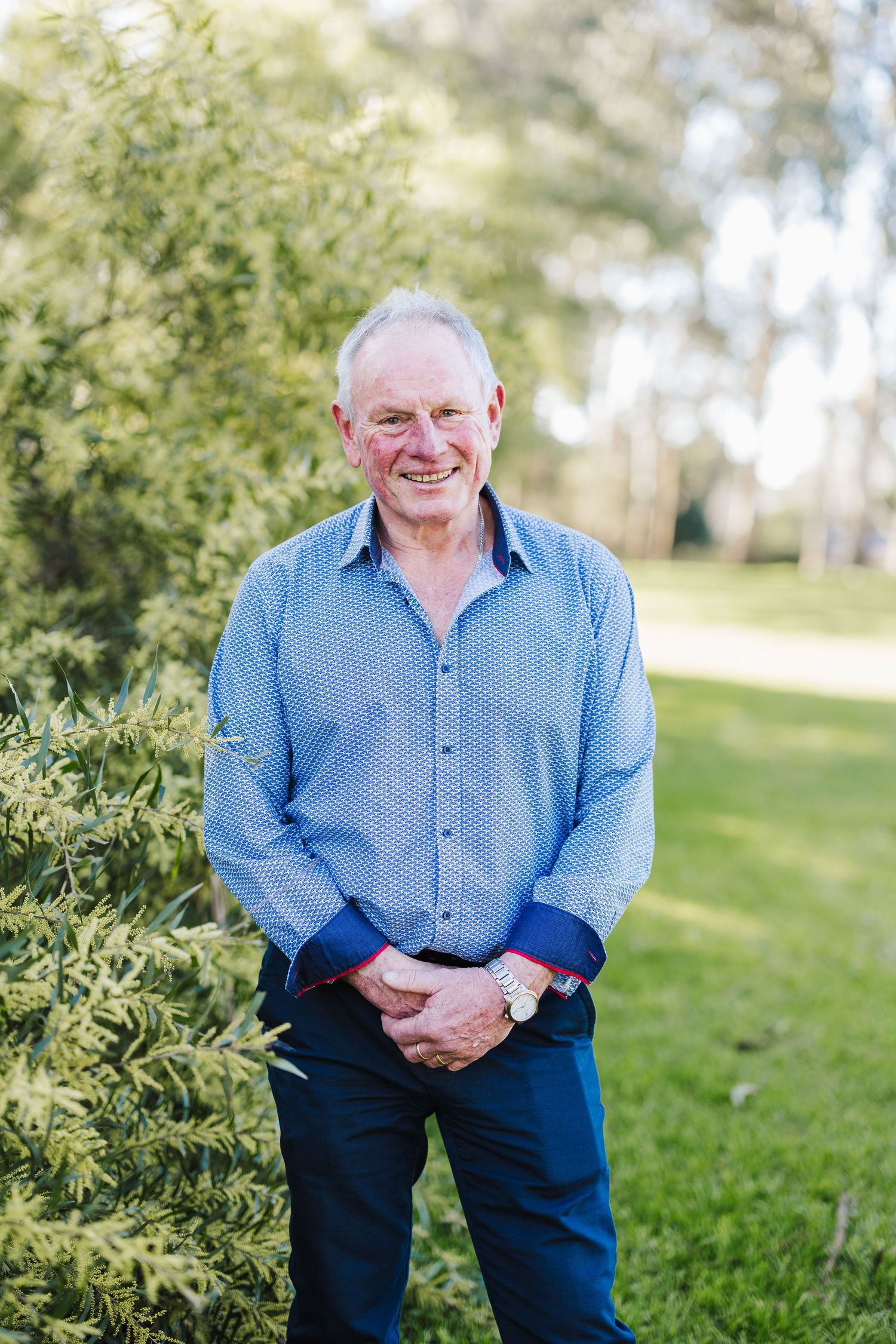 Person in blue collared shirt standing in front of green foliage outdoors.