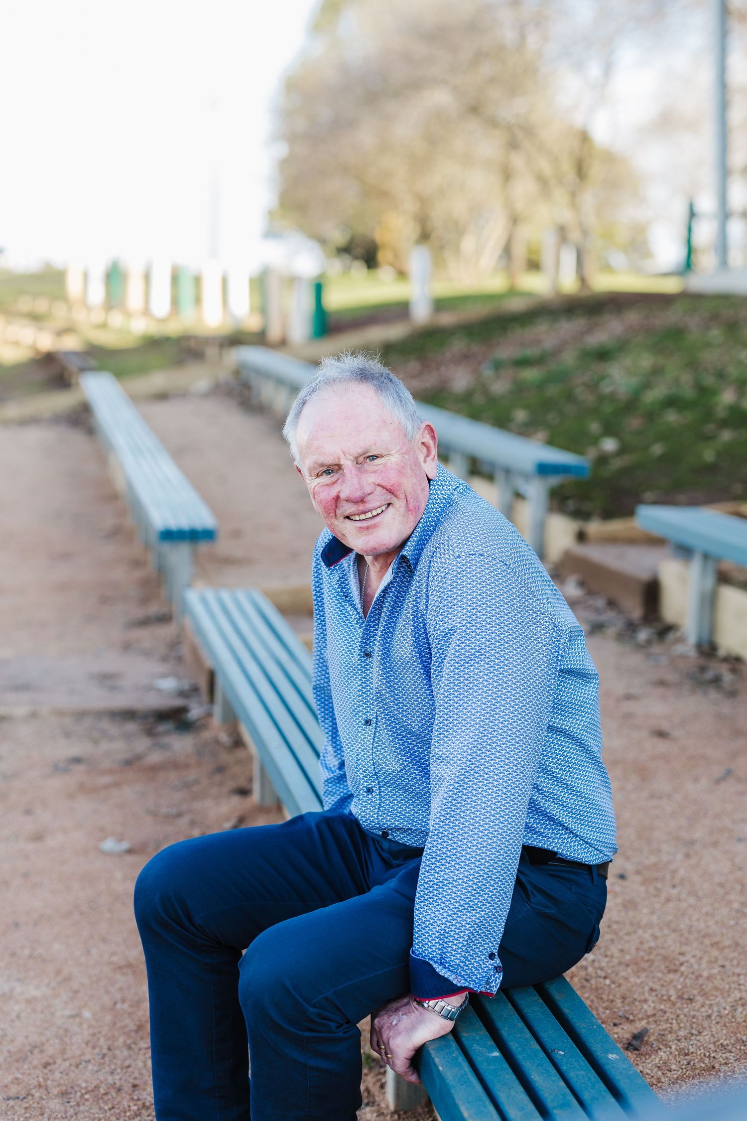Person in blue shirt sitting on a green park bench outdoors.