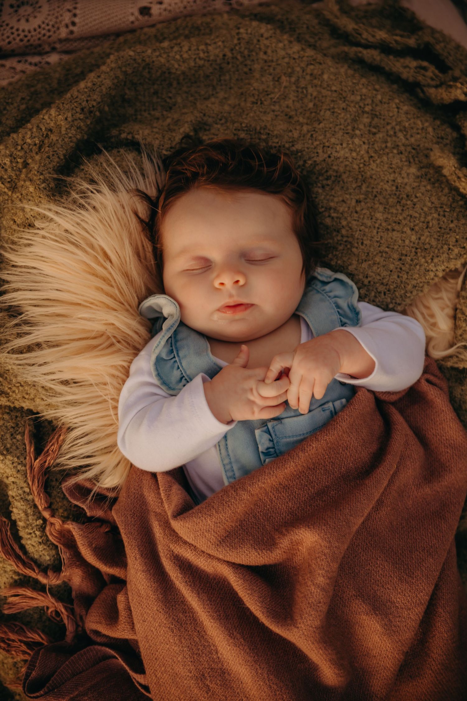 A peaceful newborn baby sleeps wrapped in a warm brown blanket nestled in a soft furry basket.