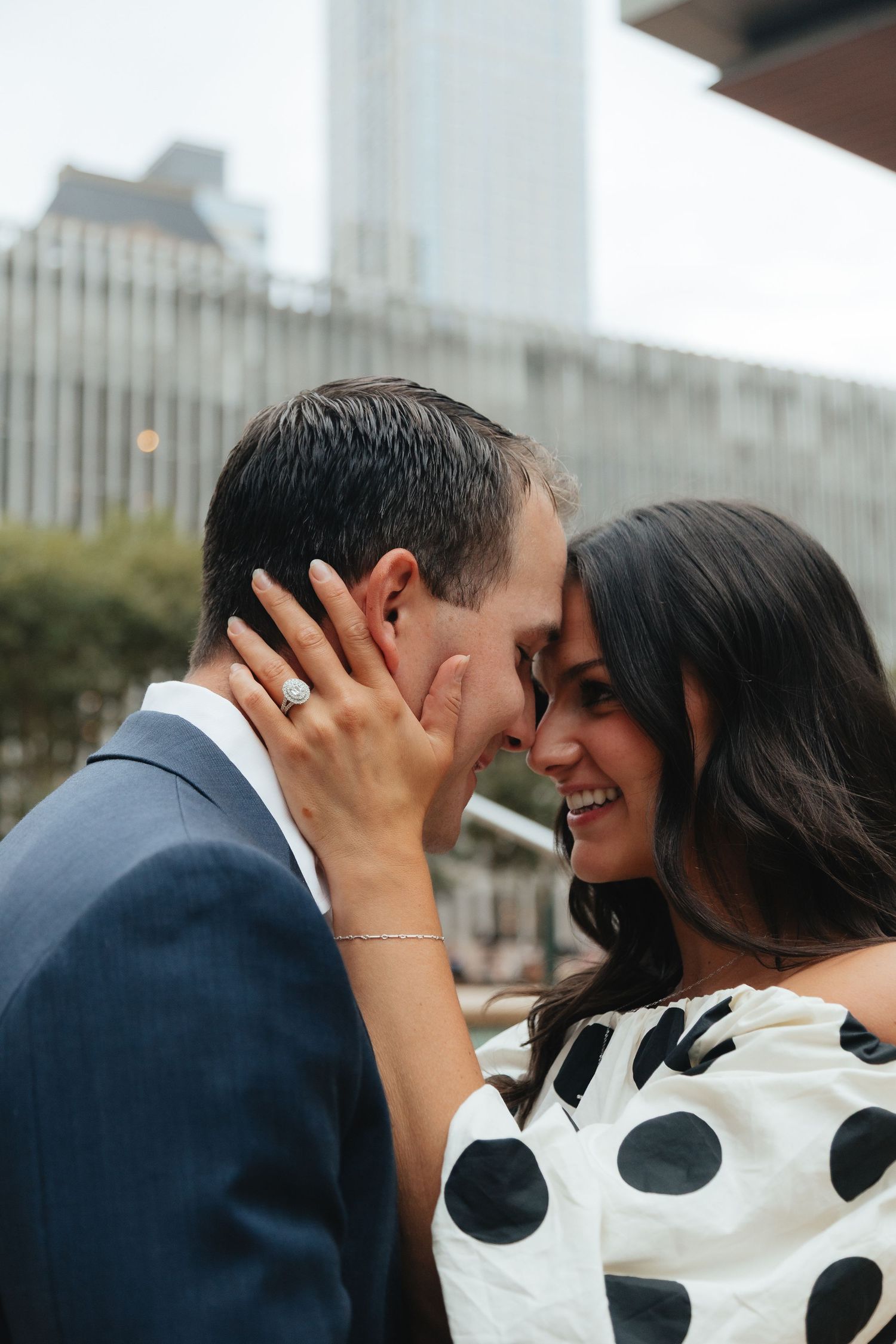 Couple shares an intimate moment outdoors, woman in polka dot dress smiling as they touch foreheads.