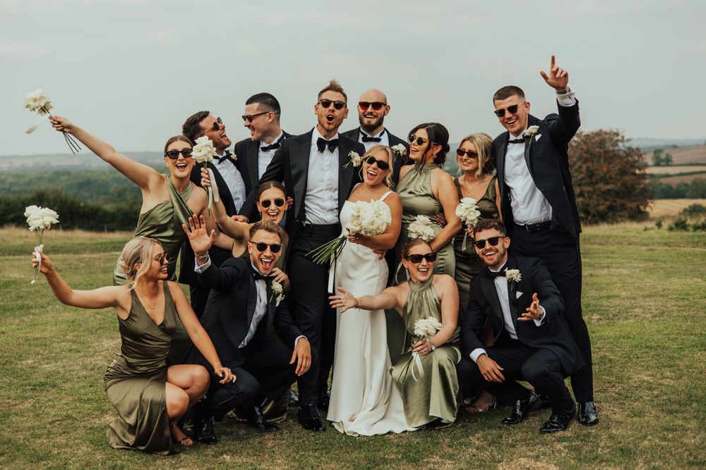 Wedding party poses for fun group photo outdoors with raised arms and celebratory gestures.