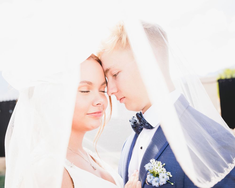 Romantic wedding photo of newlyweds sharing an intimate moment under a flowing veil.