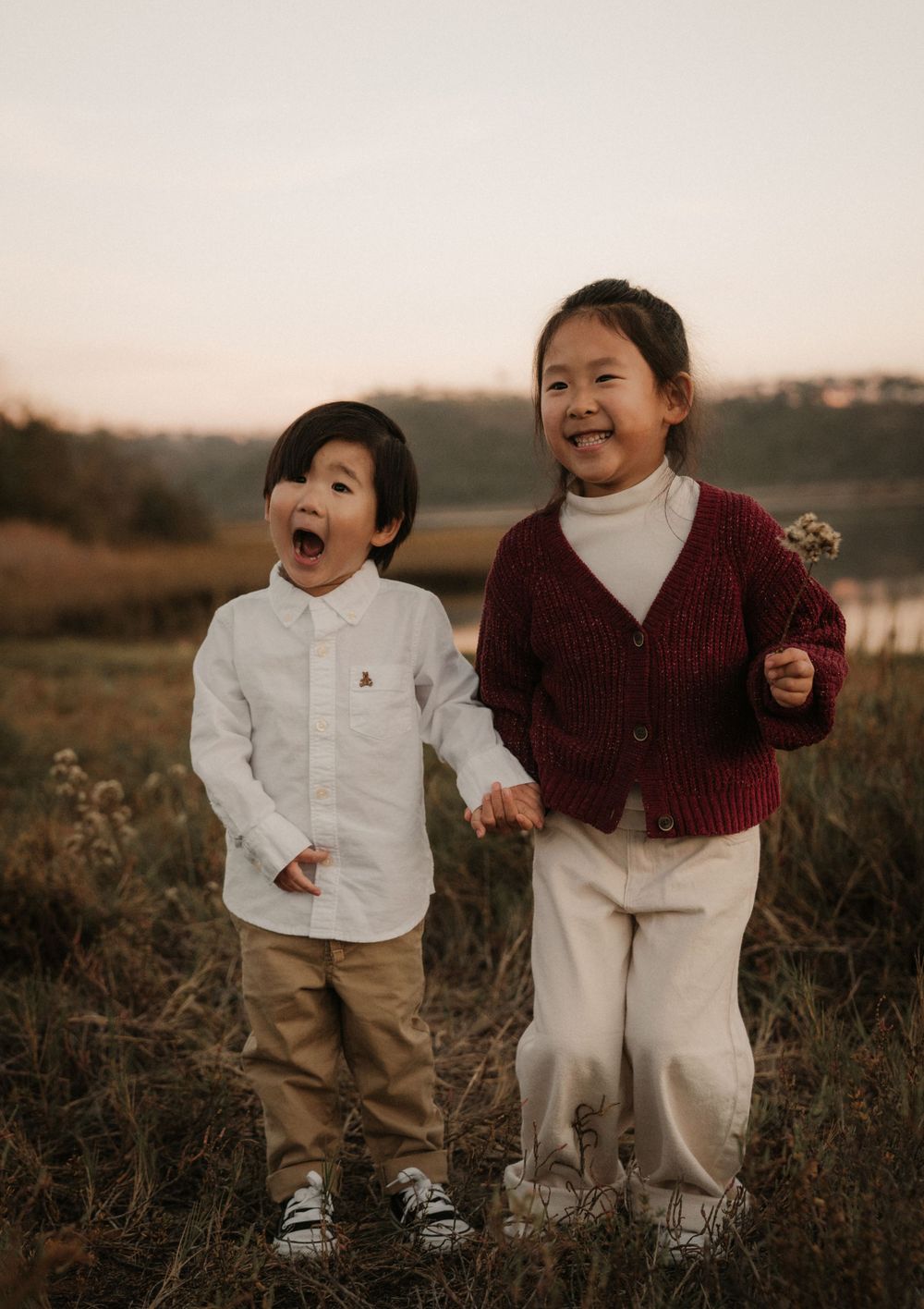 Two children laughing and playing together in a field during golden hour.