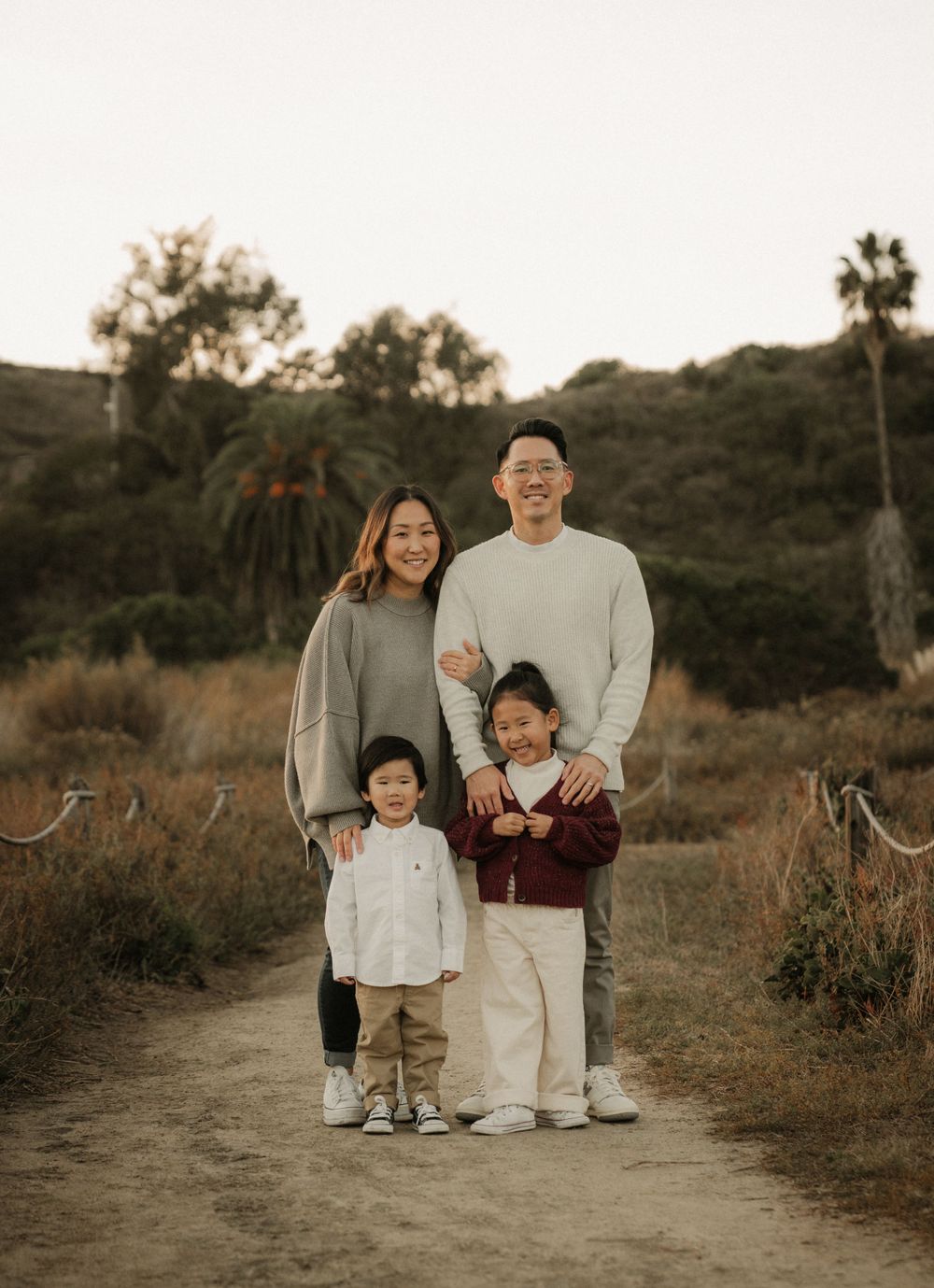 A family portrait taken on a scenic trail with palm trees and hills in the background during sunset.