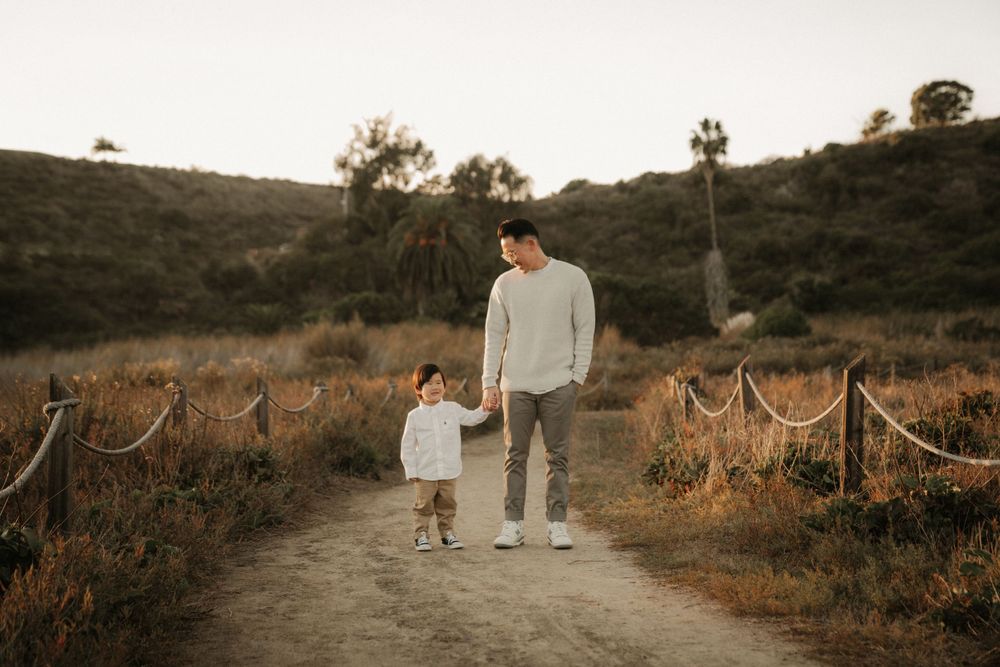 A parent and child walking together on a dirt path during golden hour in a scenic outdoor setting.