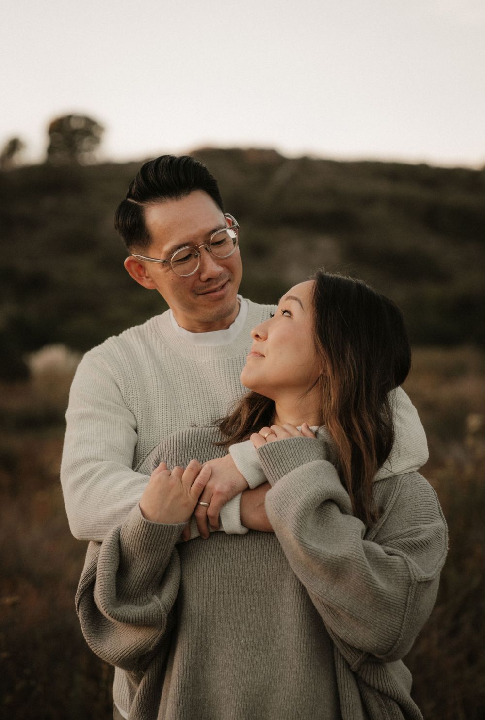 A romantic portrait of a couple in matching sweaters sharing an intimate moment at sunset.