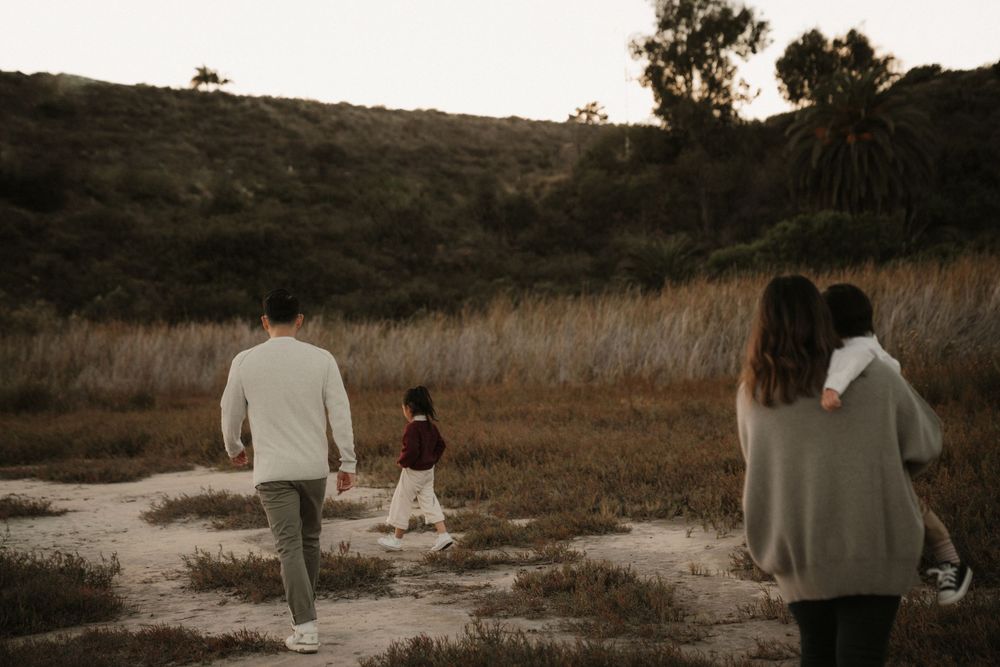 Family walking together through a grassy field at sunset in warm autumn light.