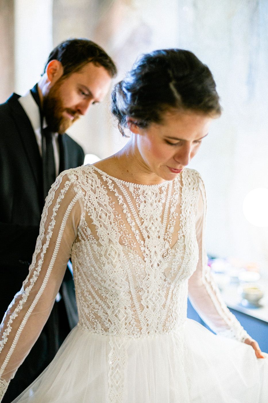 Delicate lace long sleeve wedding gown with intricate beading details shown in elegant indoor setting.