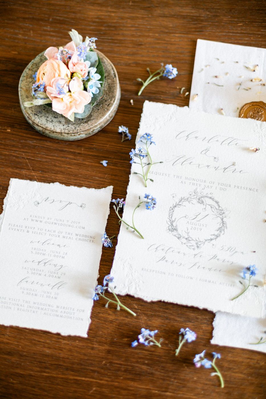 Elegant wedding invitation with handwritten calligraphy displayed with delicate blue forget-me-not flowers on wooden surface.