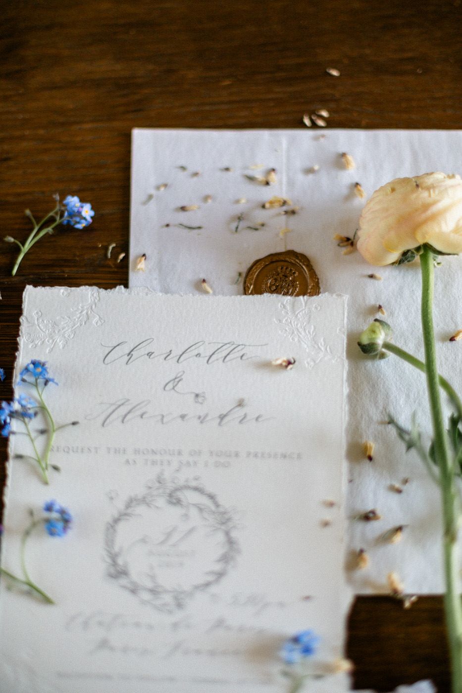 Close up of vintage style wedding stationery with delicate blue flowers and gold wax seal on wooden table.