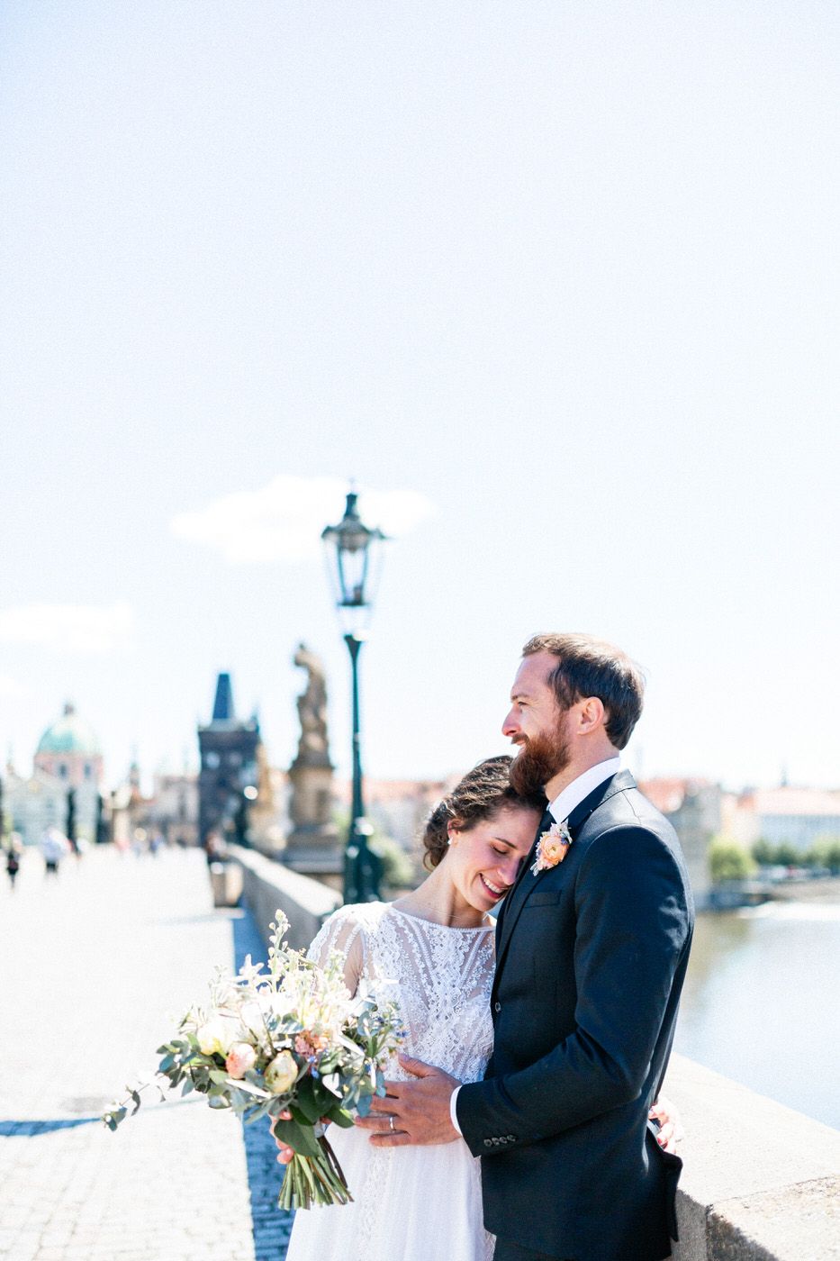 A loving couple embraces on Charles Bridge in Prague with the city skyline and historic architecture in the background.