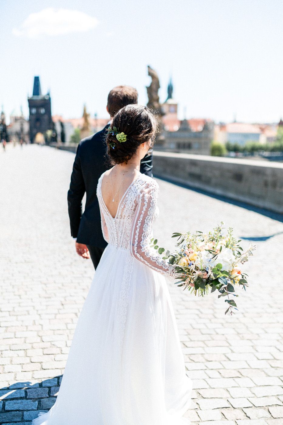 A romantic wedding scene with lace dress details and autumn bouquet on Charles Bridge in Prague.