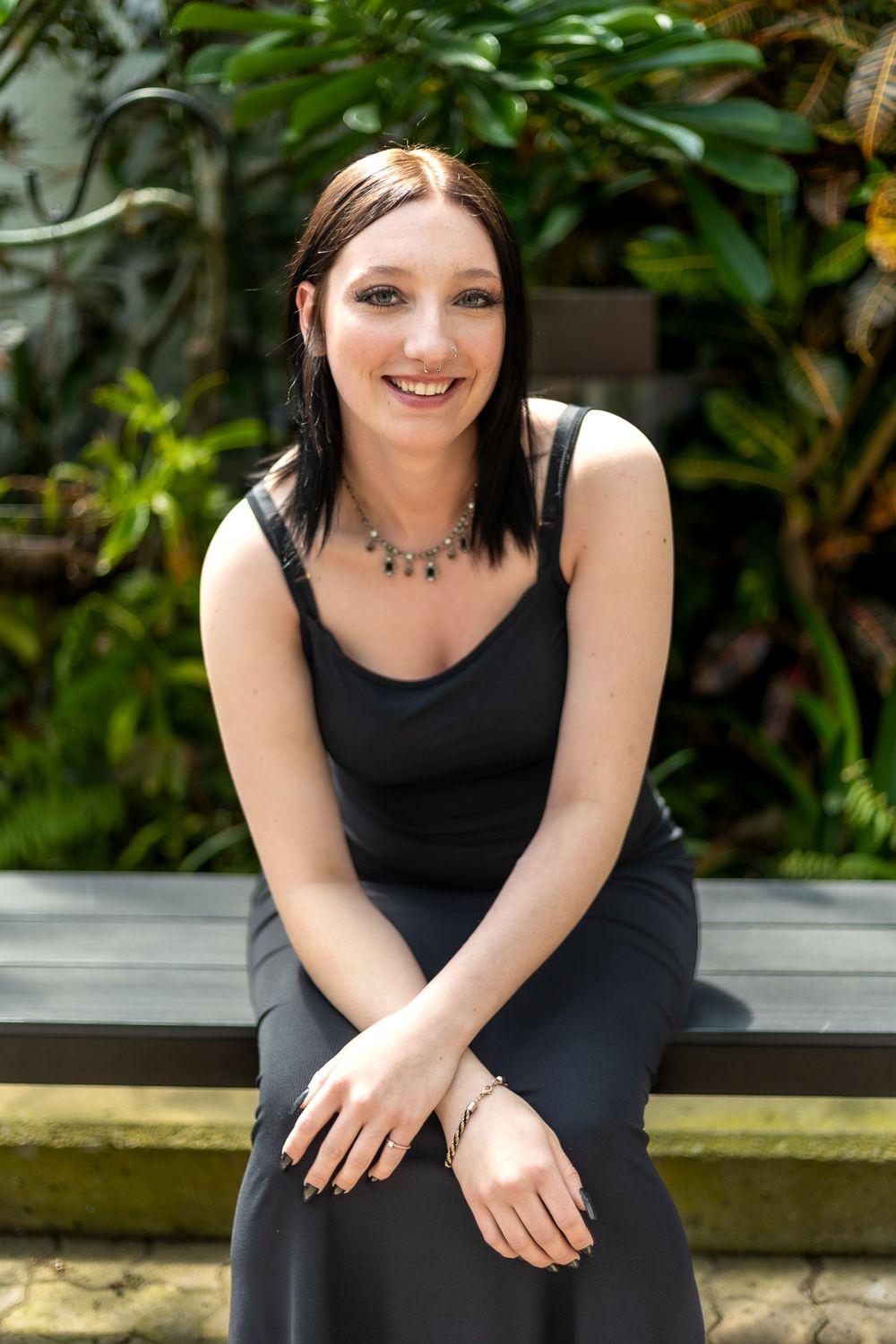 Portrait in black dress seated on bench surrounded by tropical greenery.