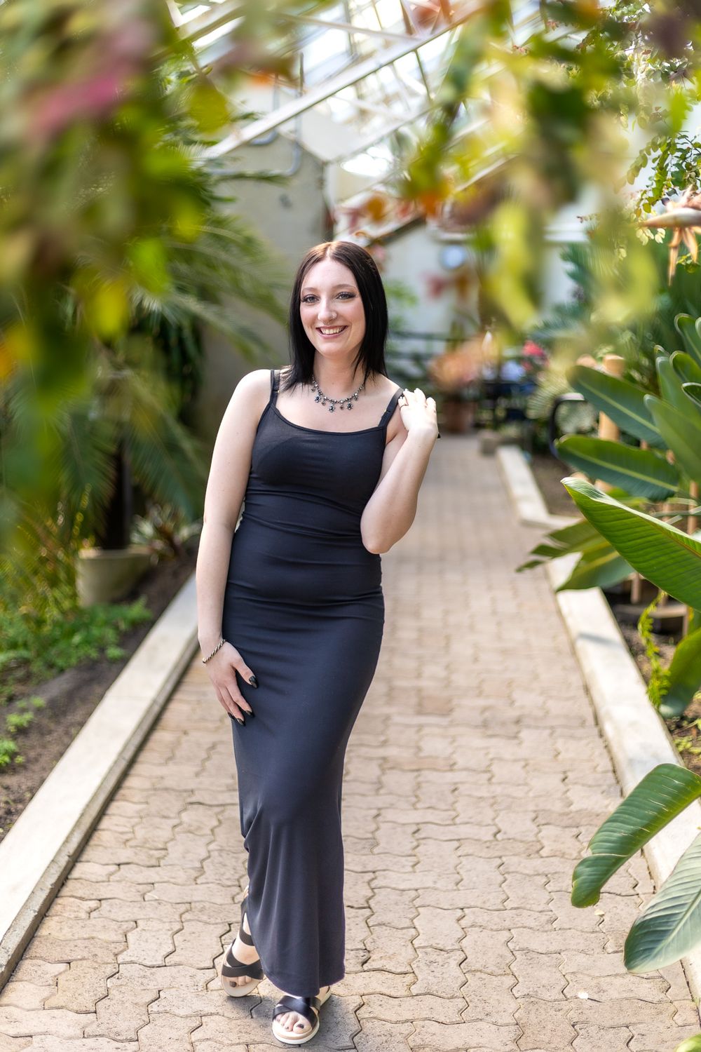 Full length photo in black dress walking along garden pathway with tropical plants.