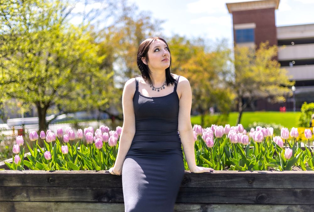 Portrait by pink tulip garden wearing black dress with parking structure visible.