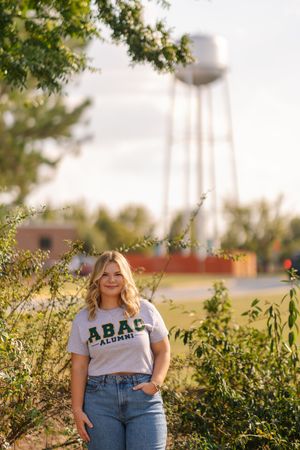 Senior portrait session in a golden field with water tower in background during sunset.