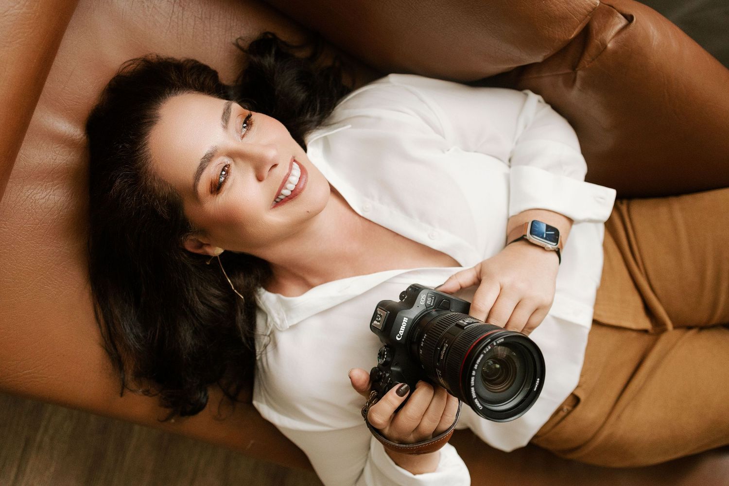 Smiling person in orange sweater holding vintage camera against white background.