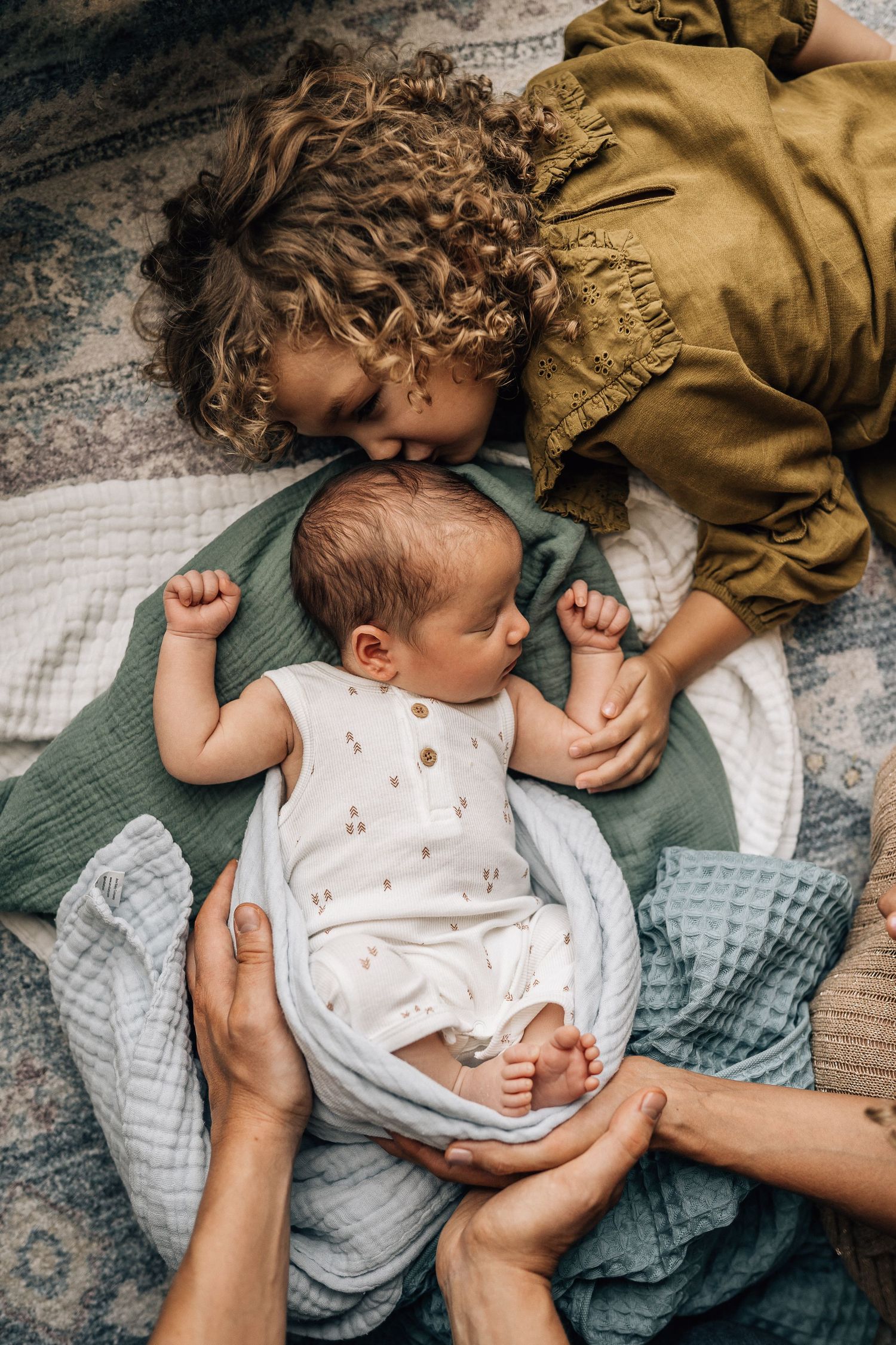 toddler girl kissing a newborn baby surrounded by mom and dad hands at dubai newborn photo shoot