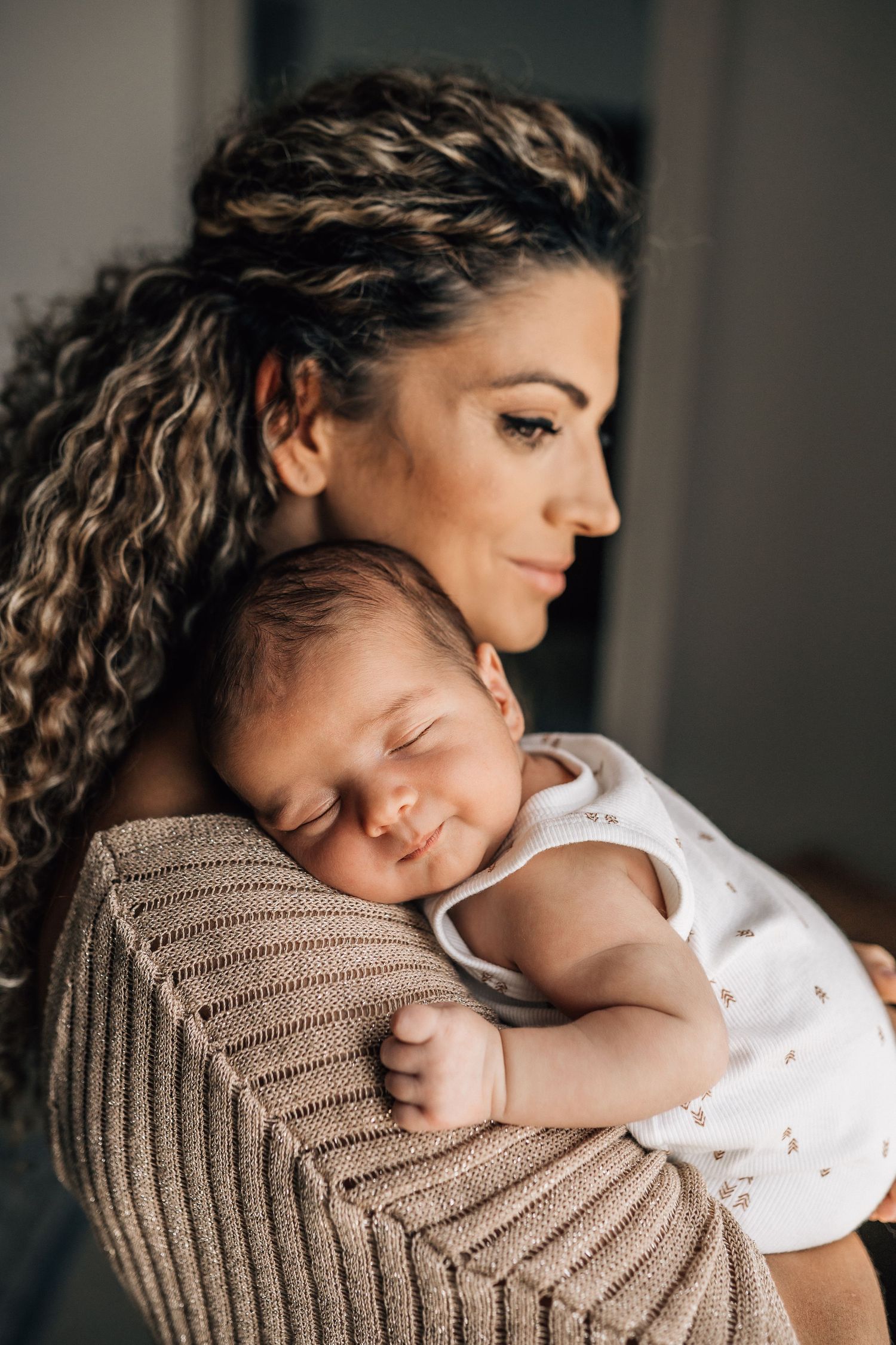 newborn sleeping on mom's shoulder while mom is watching and smiling during dubai newborn lifestyle photo shoot