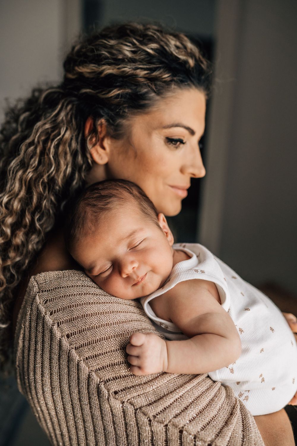 newborn sleeping on mom's shoulder while mom is watching and smiling during dubai newborn lifestyle photo shoot