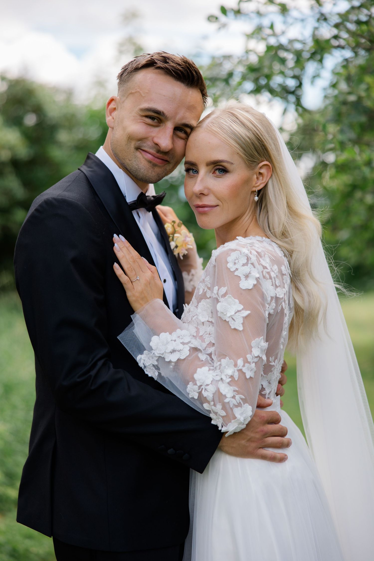 A joyful wedding portrait captured outdoors against lush greenery.