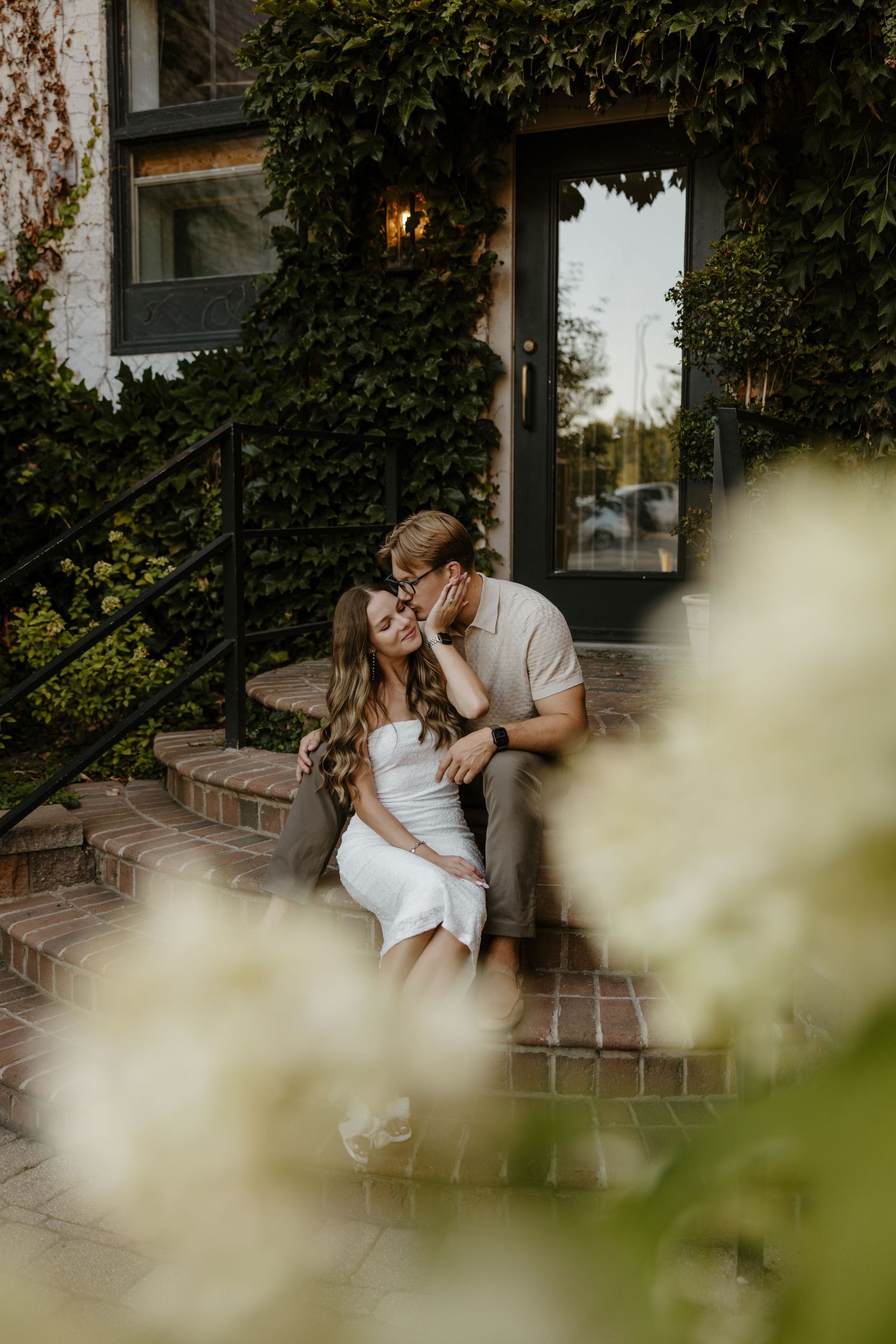 A couple embracing on a brick staircase surrounded by lush greenery and a cozy outdoor setting. Fort Worth Texas wedding photographer.