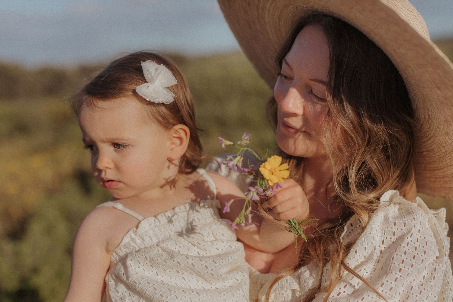 Mother and baby wearing neutral colors and hats gather in outdoor setting.
