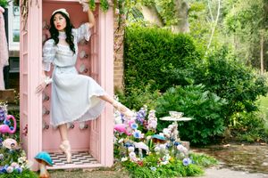 En pointe ballerina poses in pink phone both surrounded by a Alice In Wonderland inspired garden with flamingos and tea cups.
