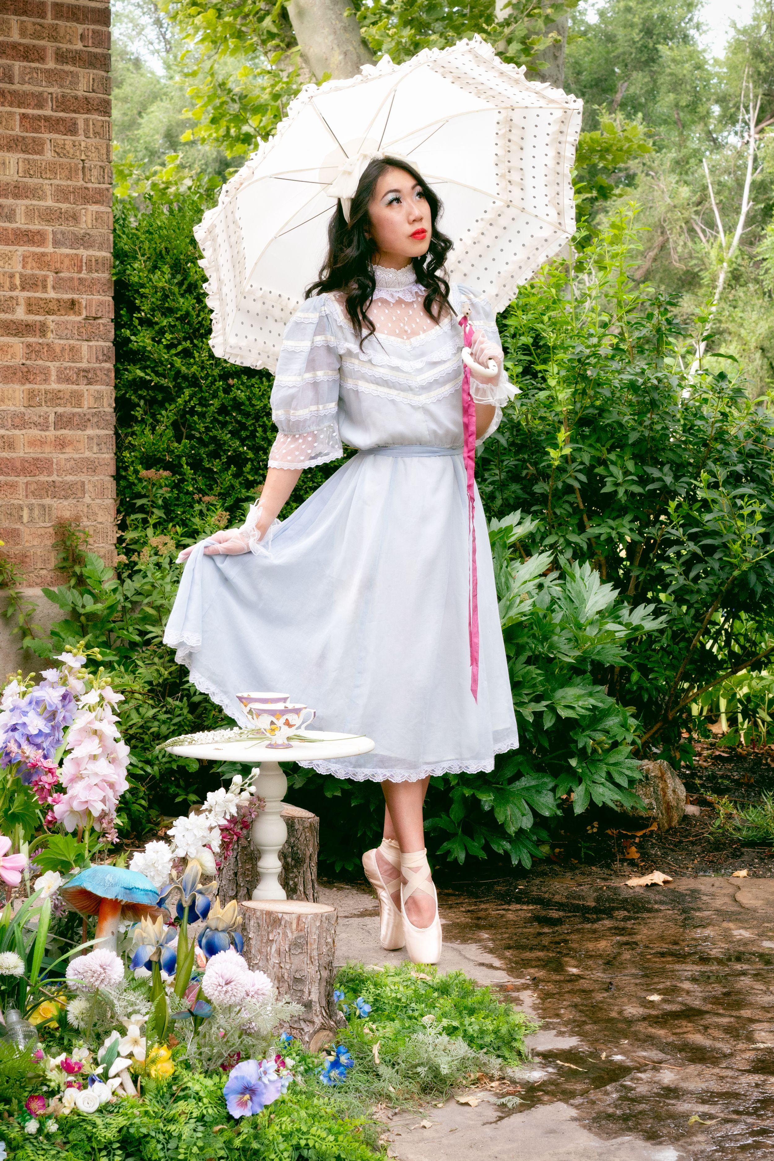 En pointe ballerina poses with a pagoda surrounded by an enchanting garden of flowers and mushrooms with flamingos and tea cups.