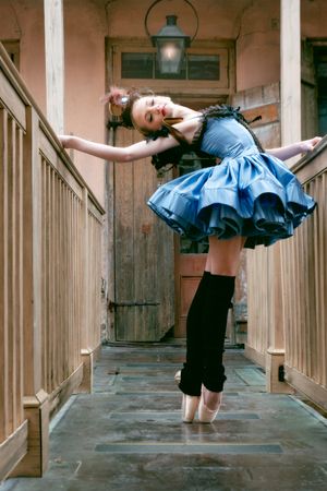 A en pointe ballerina in a blue dress with steampunk accessories performing graceful poses on a wooden catwalk in New Orleans.