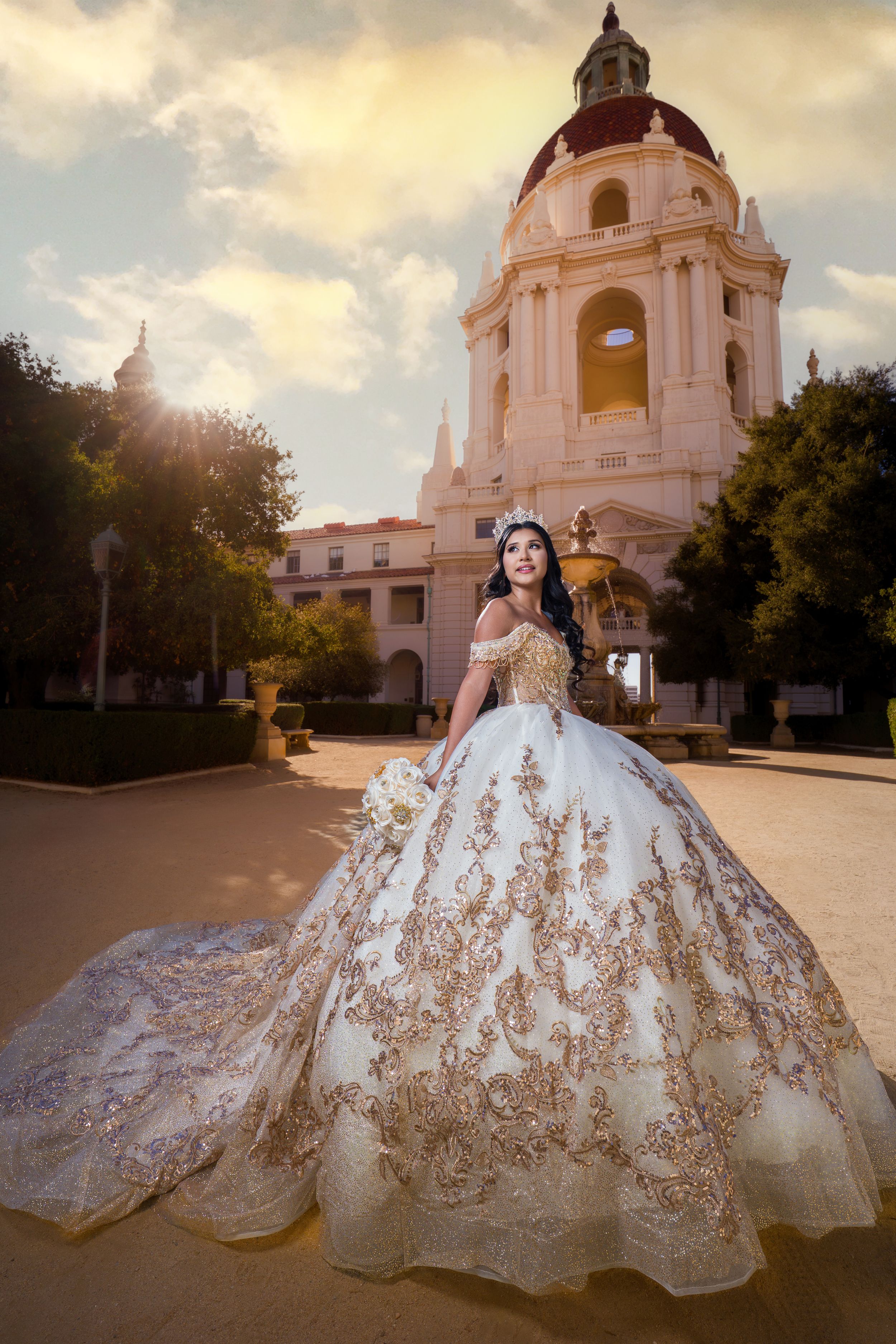 A stunning white and gold wedding gown with intricate embroidery photographed at sunset against a classical domed building.