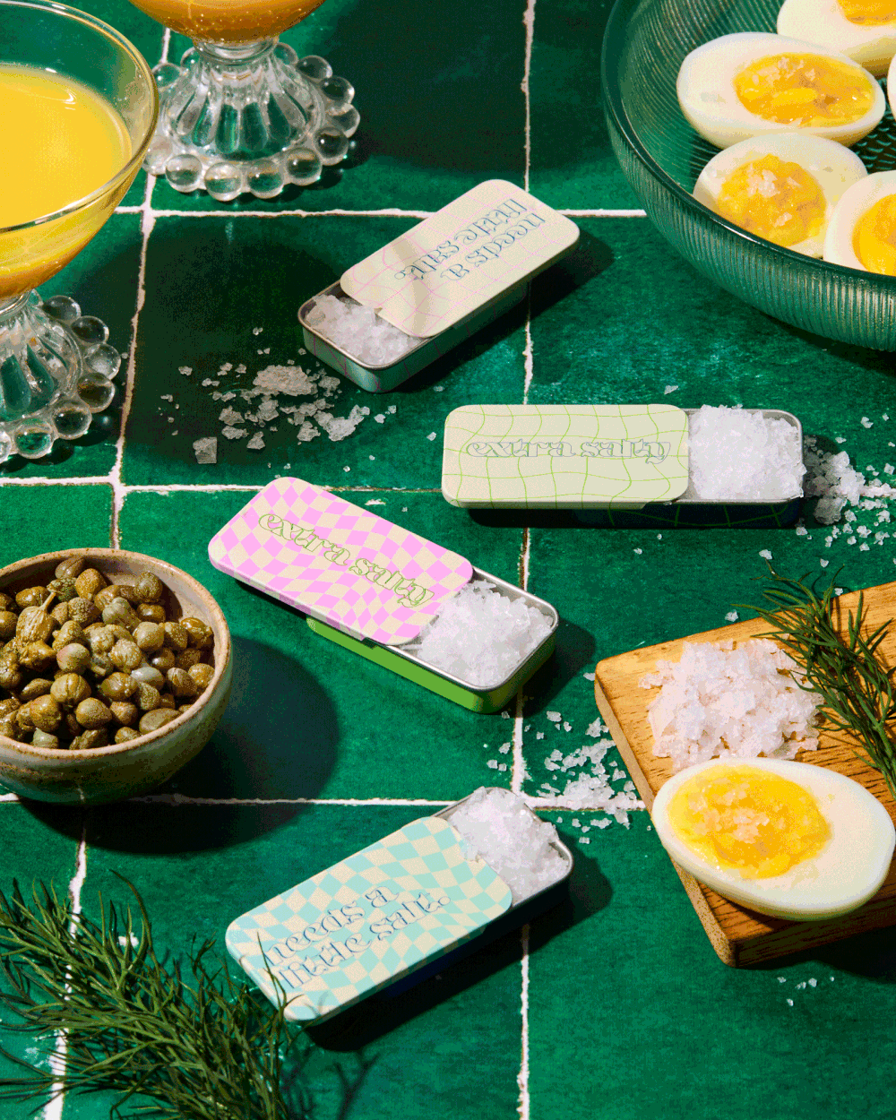 Appetizers and snacks including hard boiled eggs, capers, bread, and butter bars arranged on a green surface.
