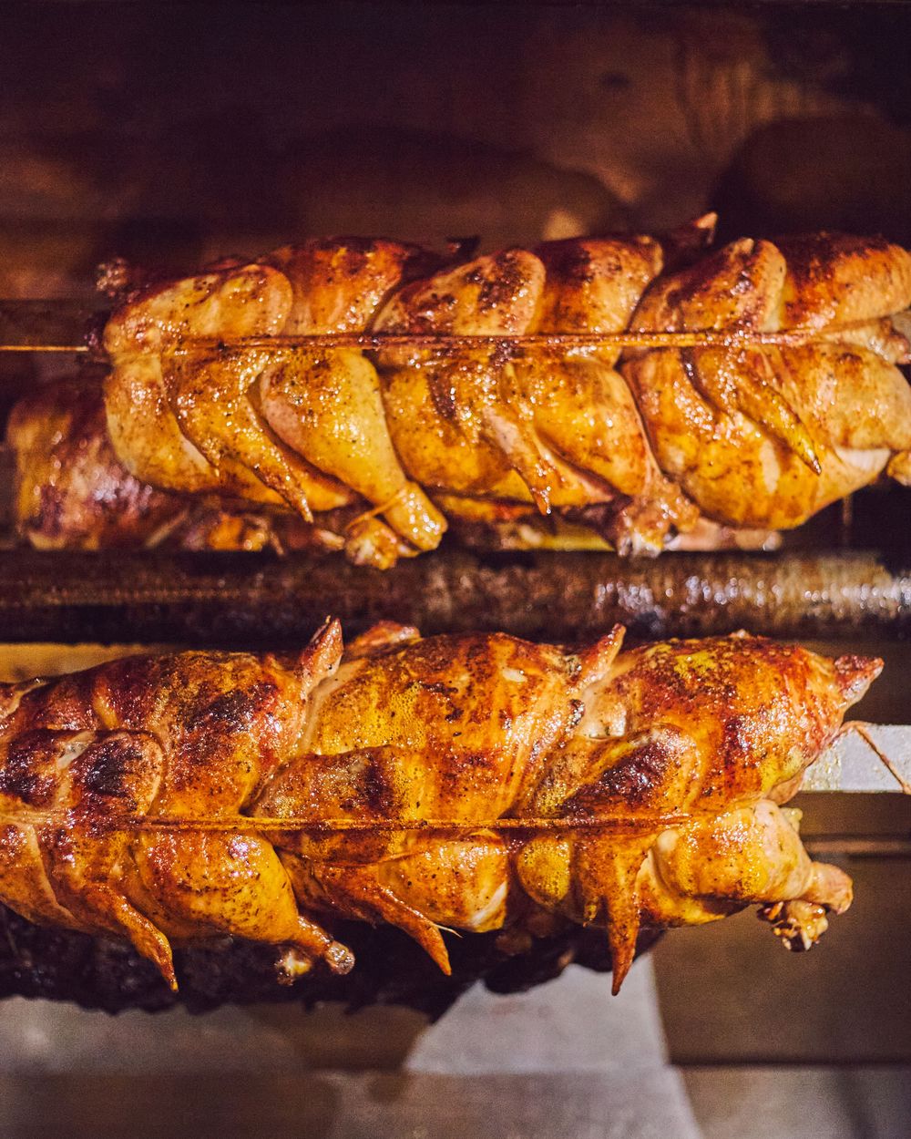 Golden roasted chickens rotate on metal spits in a rotisserie, displaying crispy, caramelized skin and glistening juices.
