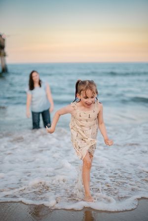 People enjoying a sunset beach walk as waves crash on the shore with soft pink sky in the background.