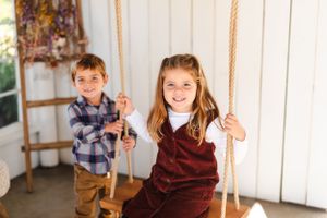 Two children playing on rope swings in a bright indoor setting with rustic decor.