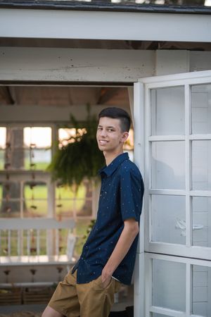 A young person in a navy blue shirt and khaki pants poses against a white gazebo structure in an outdoor setting.
